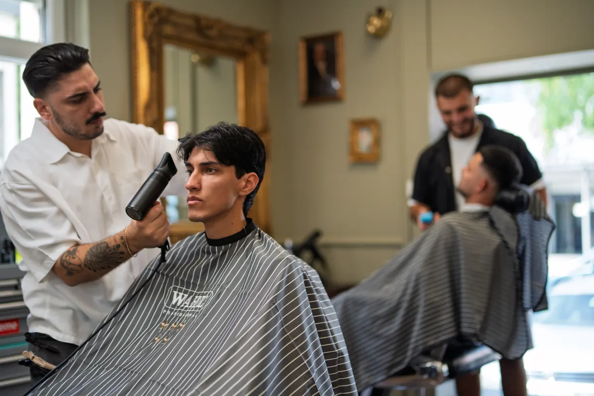 Zwei Barbiere von Der Barbier föhnen und schneiden parallel an ihren Kunden
